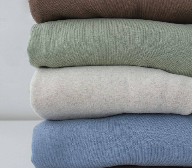 Neatly folded pastel hoodies, closet order. A stack of knitted jumpers in delicate beige, blue and light green tones. cozy fabric texture.