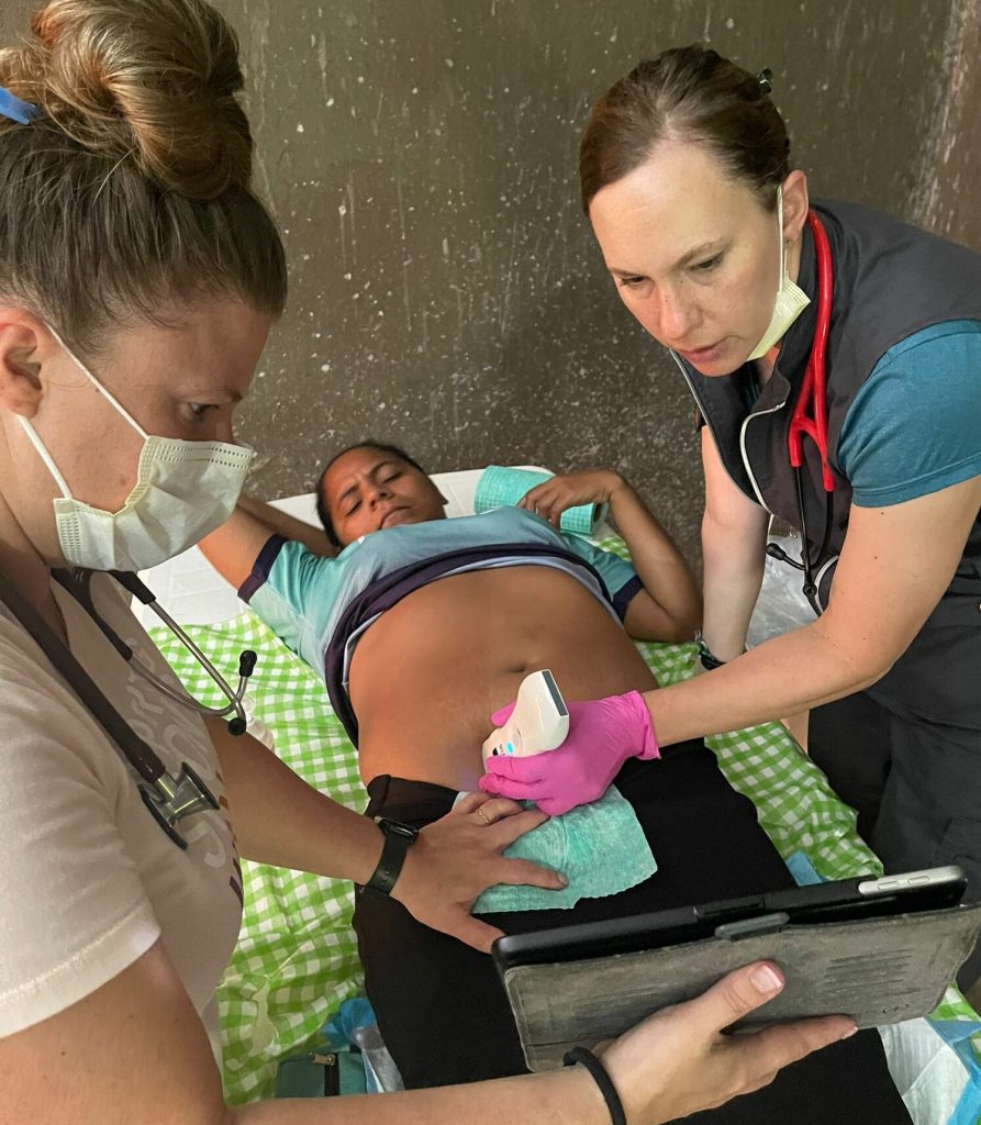 woman holding ipad while nurse uses handheld ultrasound machine to provide an anatomy scan of pregnant woman's baby